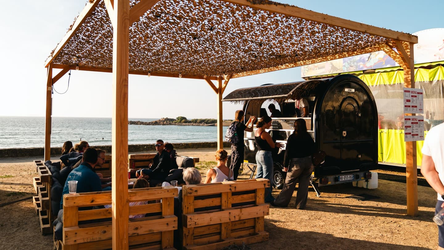 Remolque food truck en la playa, con clientes sentados a las mesas bajo la pérgola